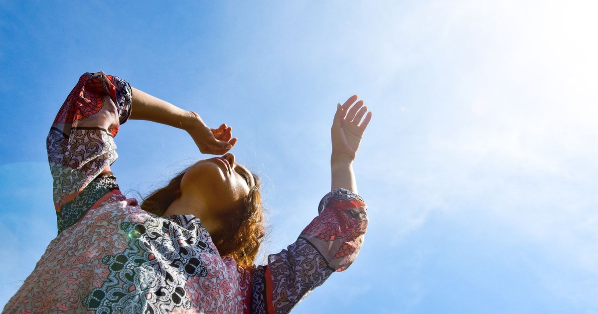 Low angle view of a woman with arms raised against a bright sunny sky.