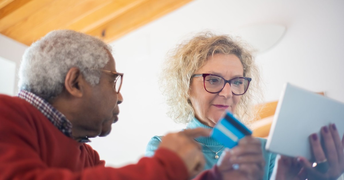 Senior adults using a tablet and credit card for online shopping indoors.