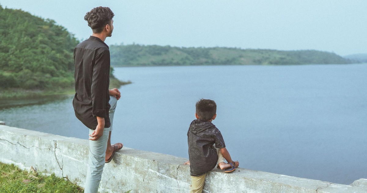 Father and son enjoying lake view amidst nature in Gujarat, India, during daytime outdoors.