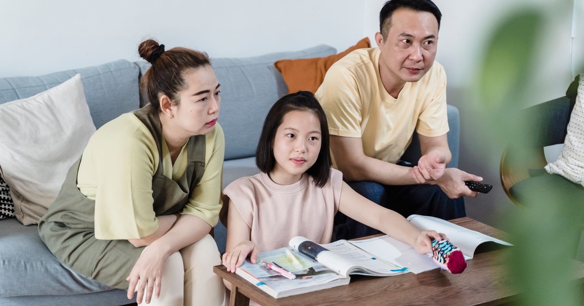 A family of three spending quality time indoors, seated on a couch with books and a remote.