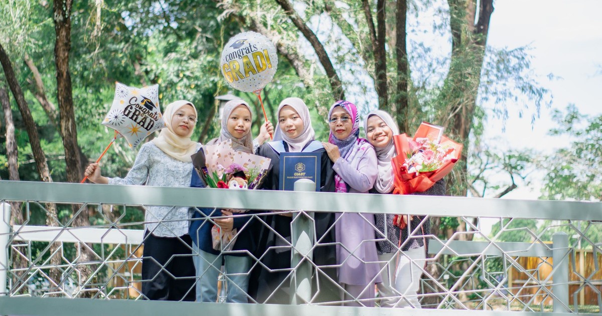 Group of women celebrating graduation with balloons and flowers outdoors.