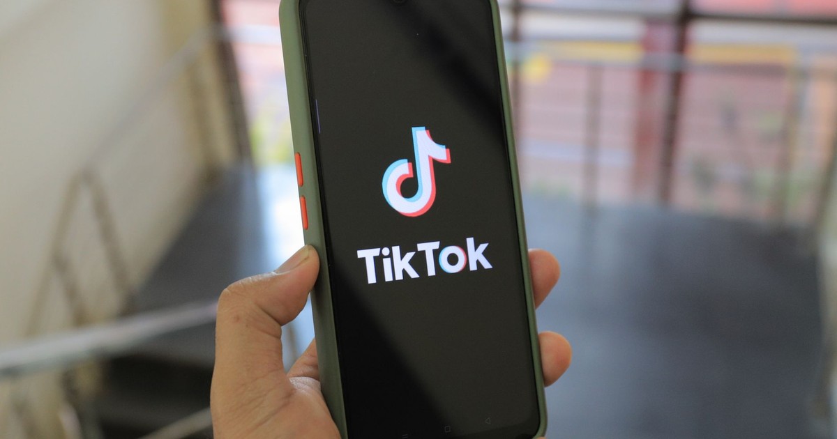 Hand holding a smartphone showing the TikTok app screen in an indoor setting.