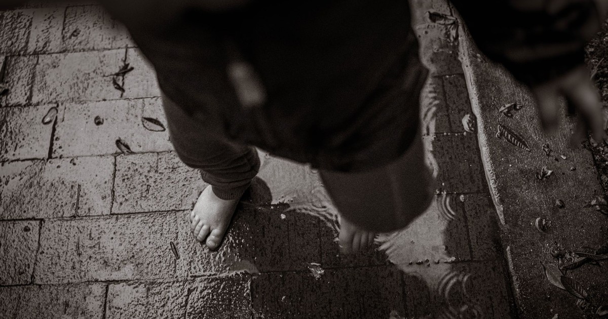 A child playing barefoot in a puddle on a wet, textured brick path.