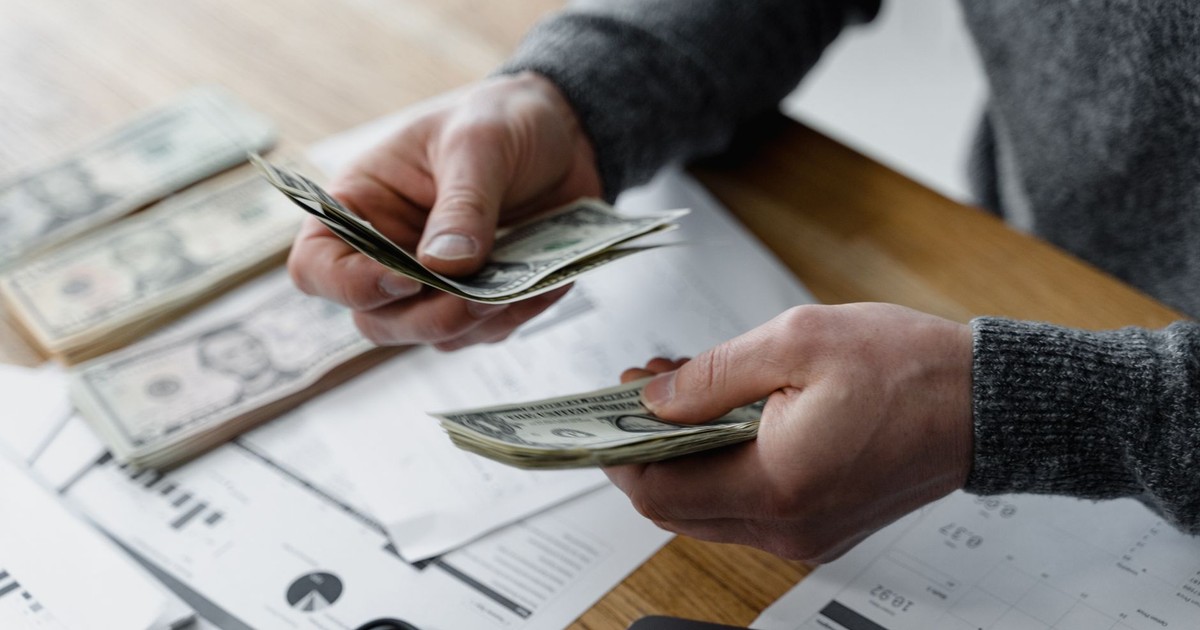 Person counting dollar bills on a desk with financial documents and a calculator in the background.