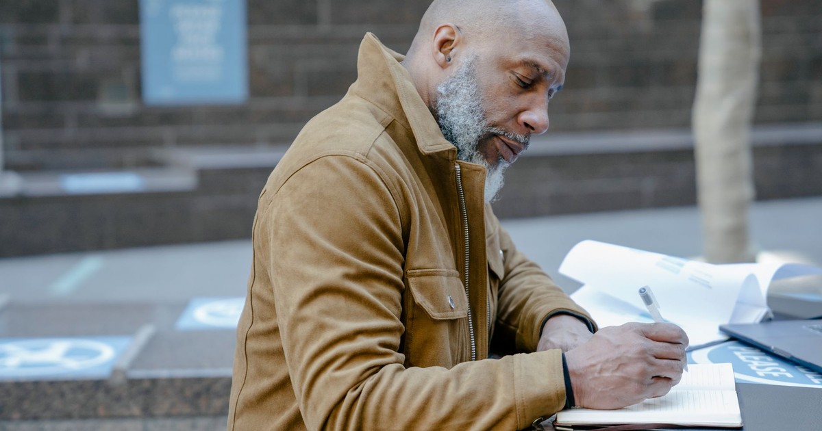 Mature businessman writing notes outdoors in a city setting, highlighting urban lifestyle and work.
