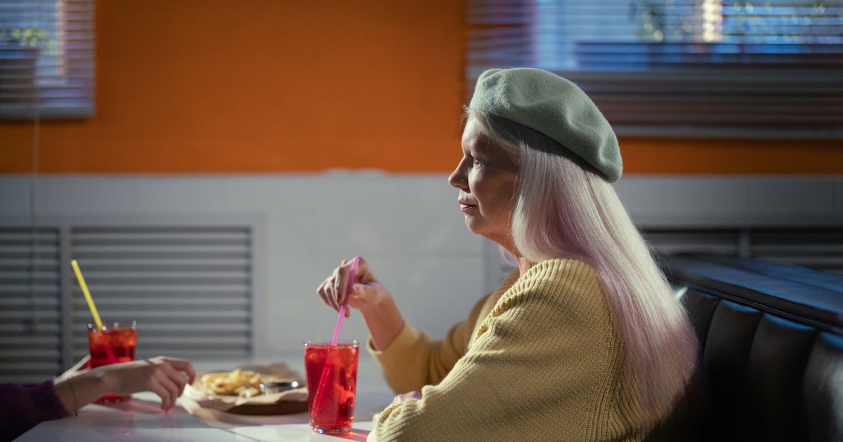 Stylish senior adult in beret and cardigan having a drink, embodying timeless fashion.
