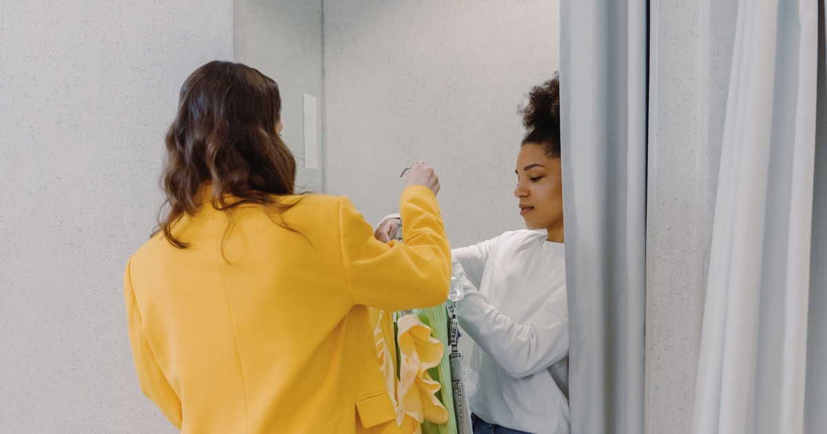 A personal stylist helps a client with clothing choices in a fitting room, focusing on fashion styling.