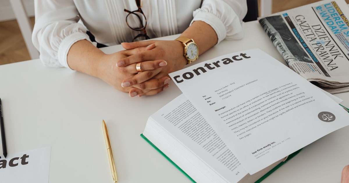 Businesswoman sitting at desk reviewing contract with legal documents and newspaper.