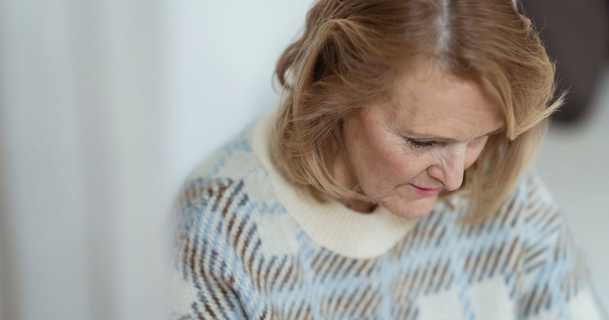 Crop positive middle aged lady with blond hair in stylish sweater smiling and looking down in daylight