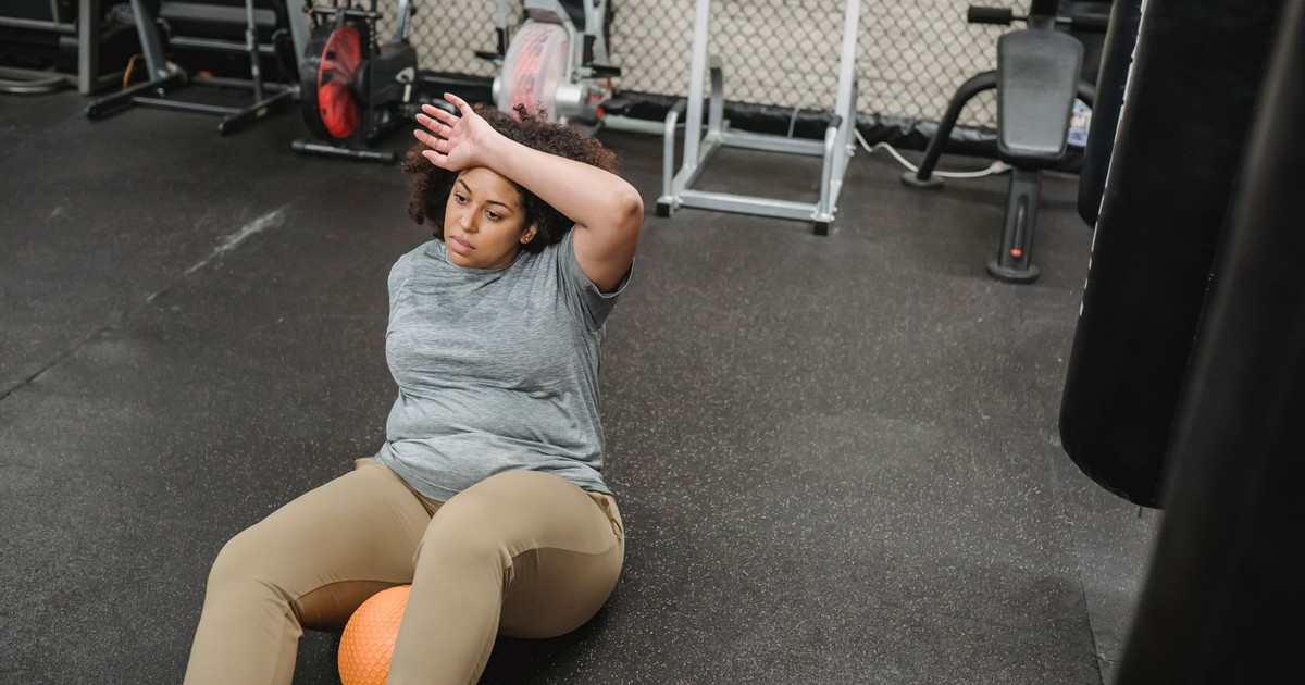 From above of exhausted African American female with ball resting after working out on floor in gym