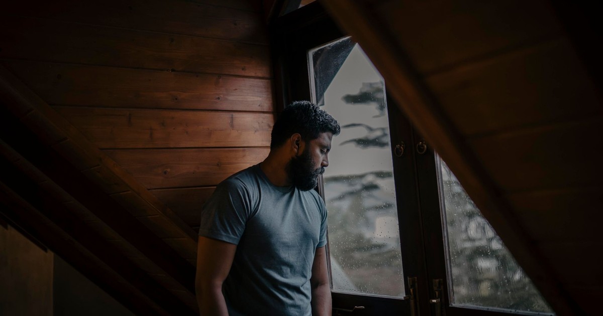 A thoughtful man stands by a window, lost in contemplation, indoors in Sri Lanka.