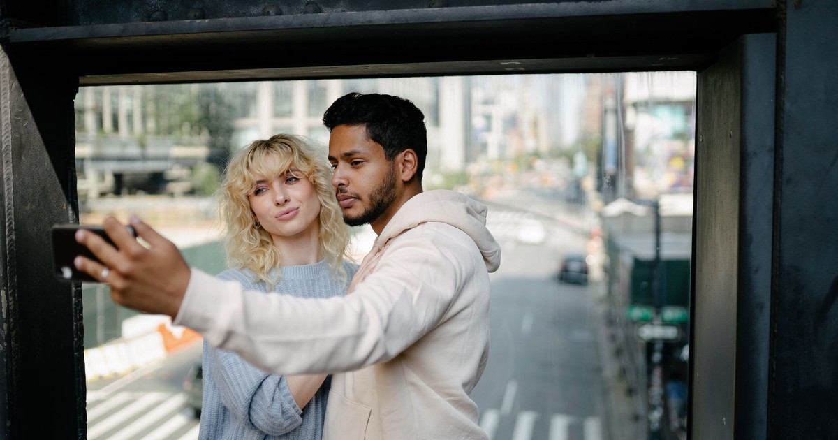 A young couple taking a selfie on a bridge overlooking a city street.