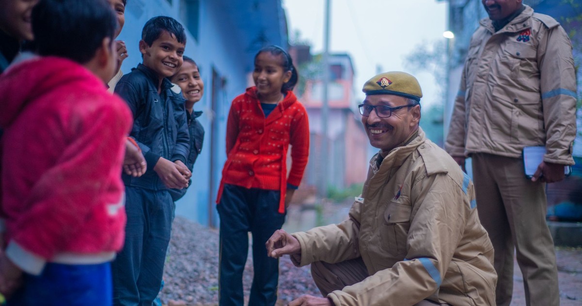 Friendly police officers interacting with smiling children in a street in Uttar Pradesh, India.