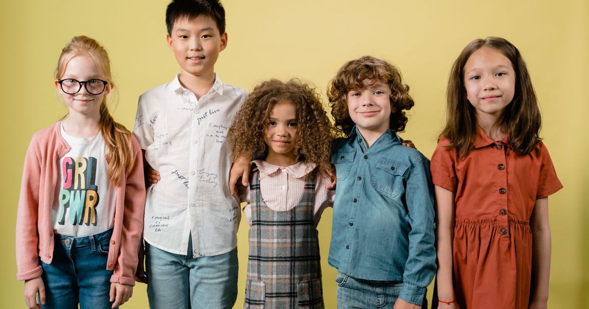 Five diverse children smiling against a yellow background in a studio setting.