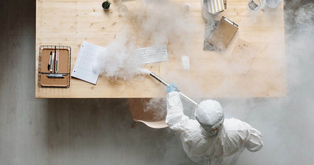 An individual disinfects a workspace using fumigation, wearing full protective gear for safety.