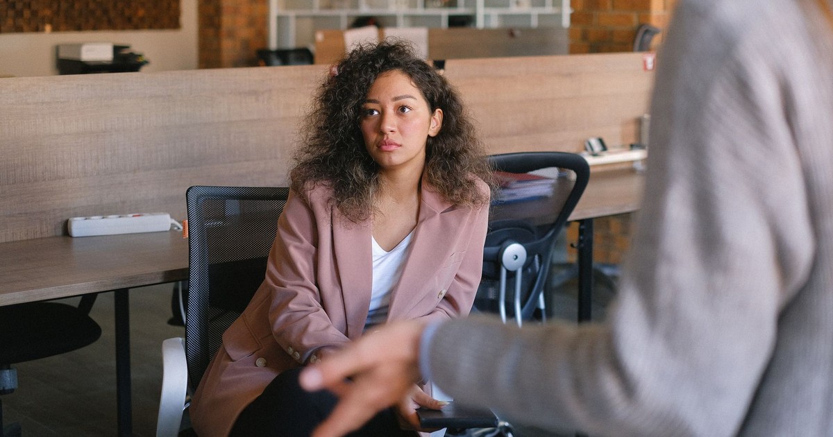 Attentive female manager sitting on chair and listening to report of coworker during business discussion in office