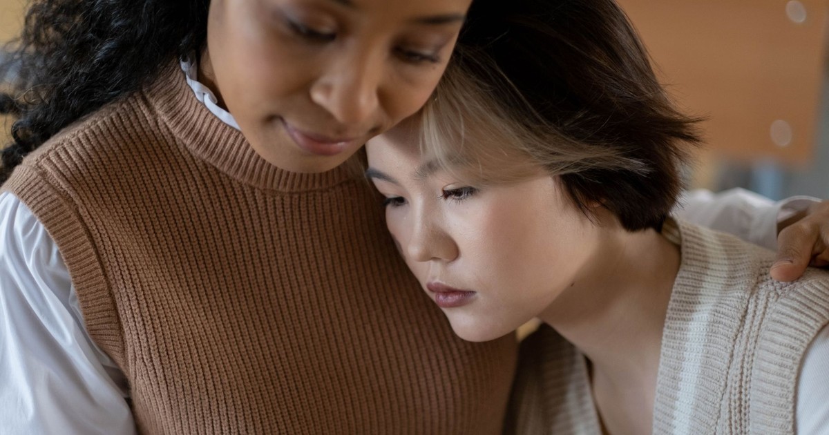A tender moment of support between two women indoors, conveying care.