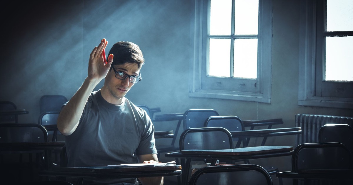 A student raises their hand in an empty classroom with dramatic lighting.