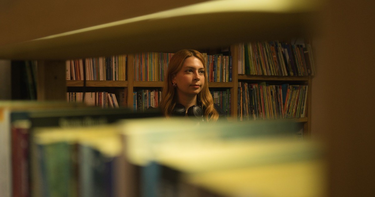 Young woman in a library looking thoughtfully through book shelves.