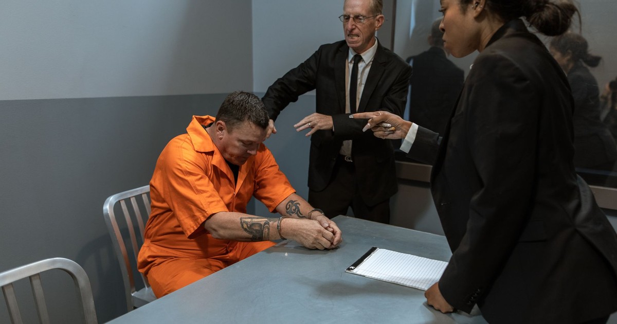 A tense interrogation scene with officers and a prisoner in an orange jumpsuit.
