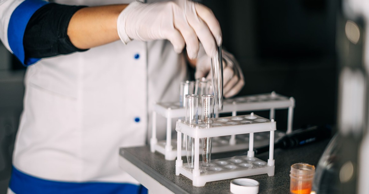 A scientist in a lab coat handling test tubes in a laboratory setting with a focus on equipment.