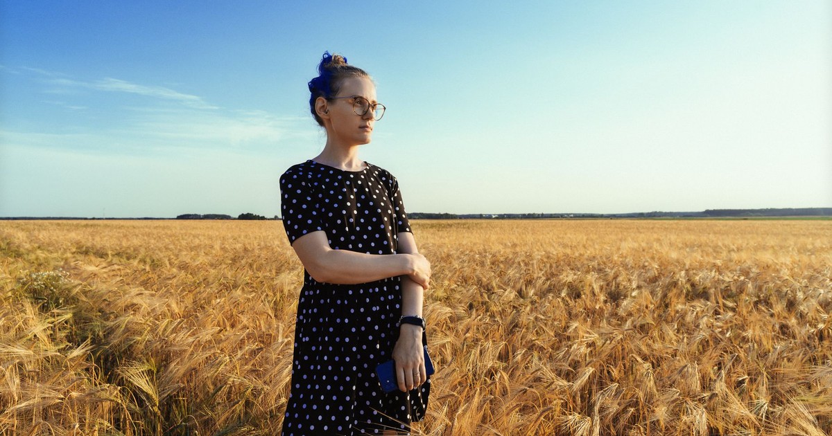 A woman in a polka dot dress stands in a golden wheat field on a sunny day.