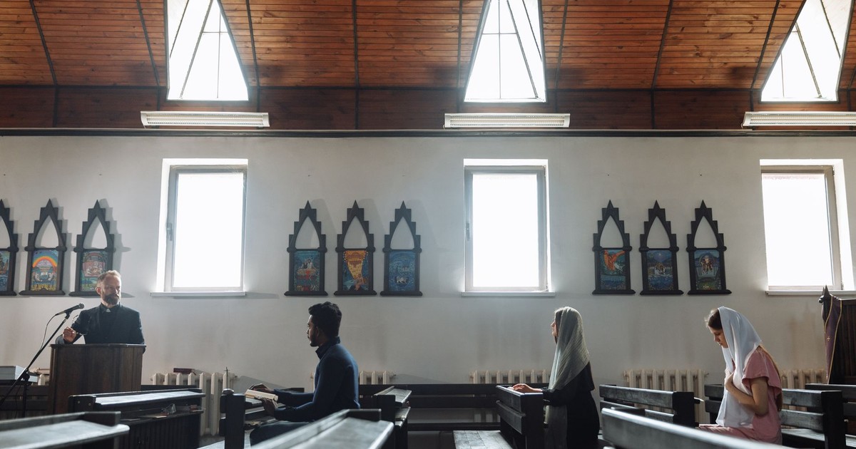 A serene church interior with people praying and a priest presiding from a pulpit.