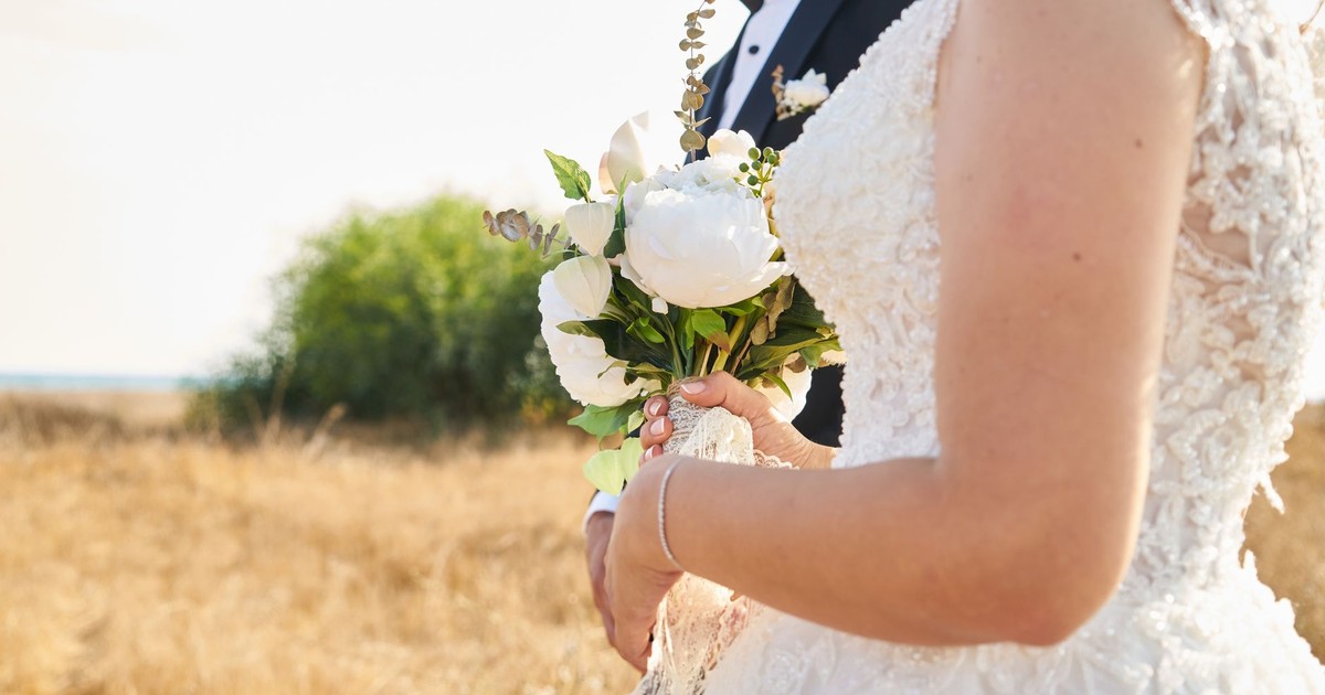 Bride and groom in elegant attire holding a bouquet in a scenic outdoor setting.