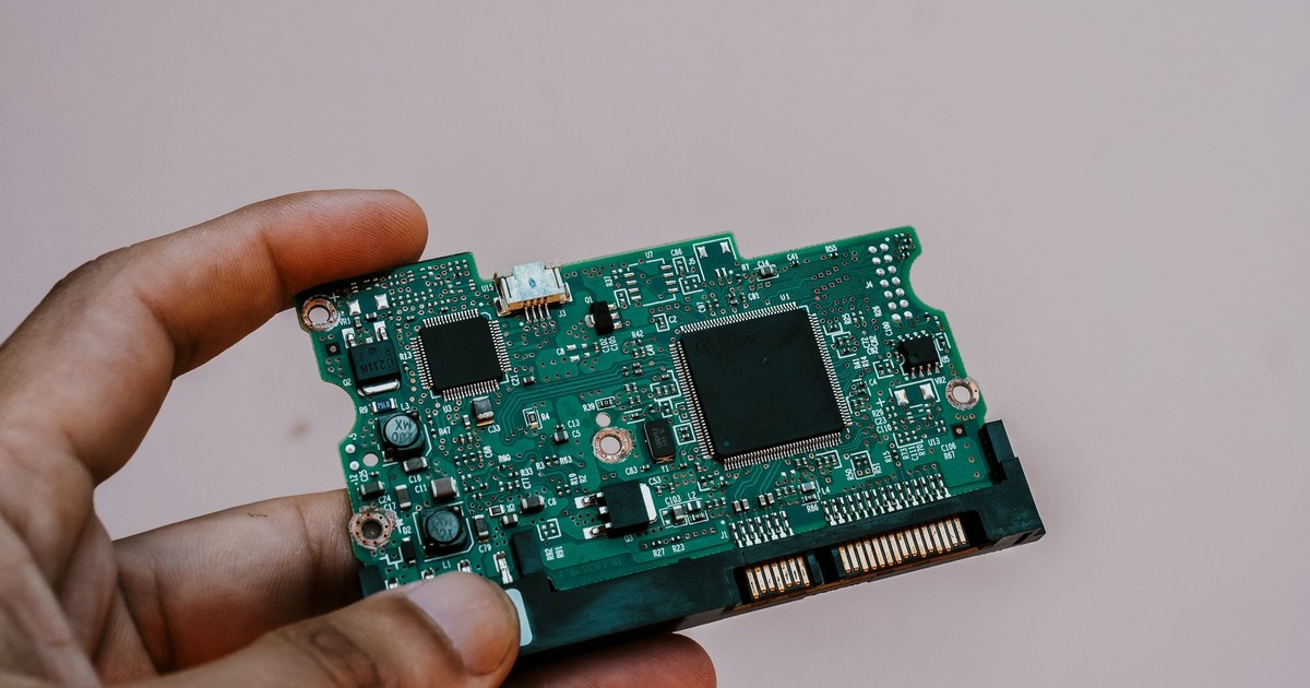 Close-up image of a hand holding a circuit board from a hard drive, showcasing electronic technology.