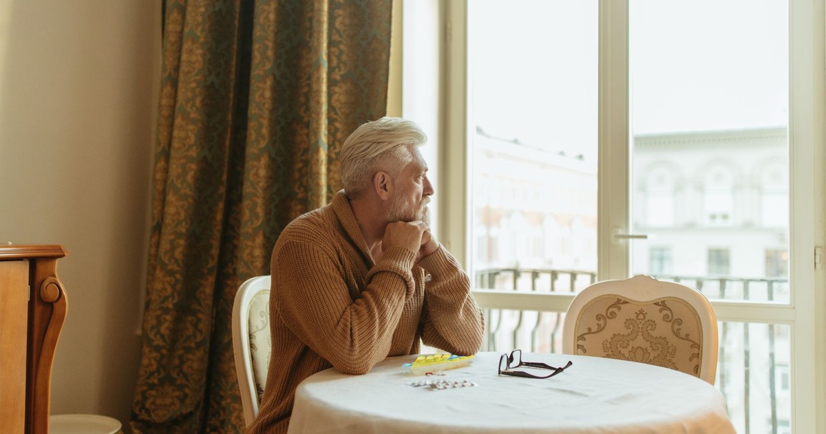 Elderly man in a cozy room gazing thoughtfully out the window during the day.