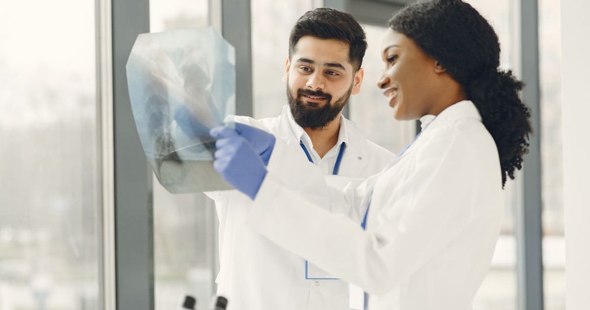Two doctors in lab coats examine an X-ray image in a bright medical facility.