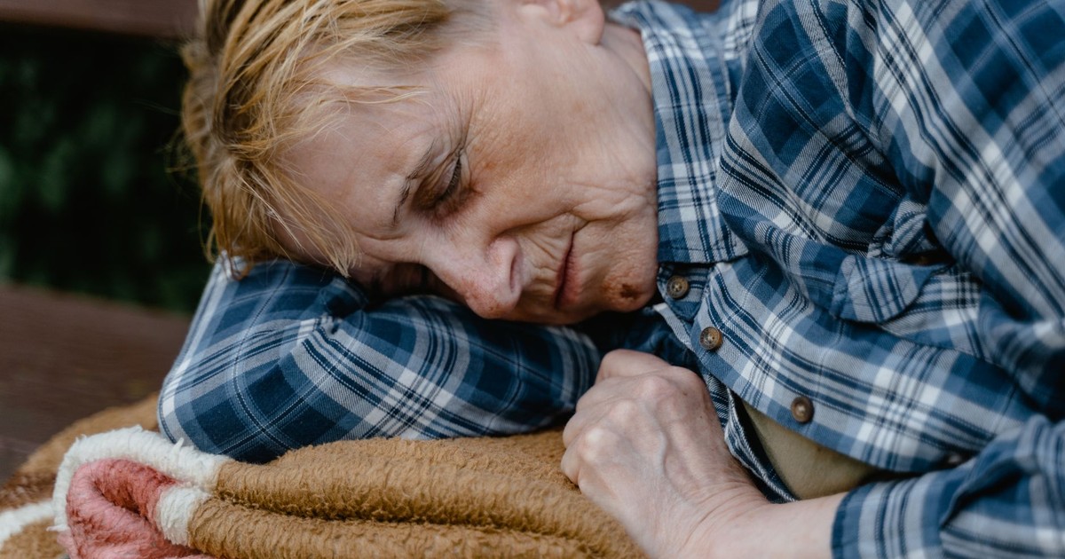 Close-up of a serene elderly woman sleeping outdoors on a bench, wrapped in a blanket.
