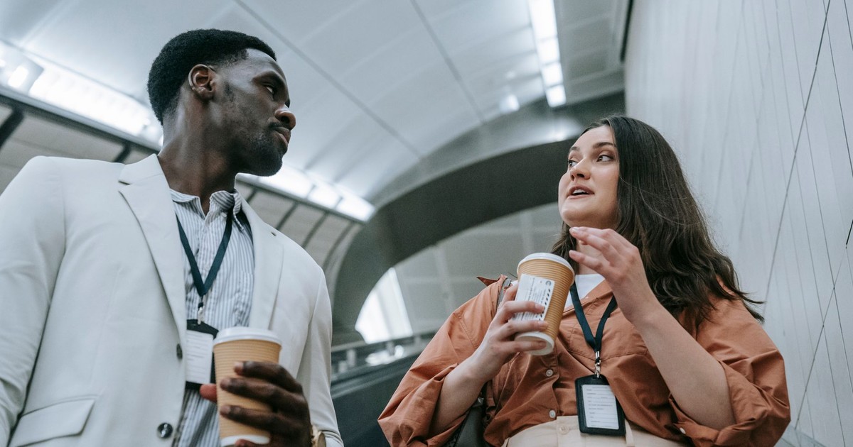 Two business professionals conversing casually on an escalator while holding coffee cups.