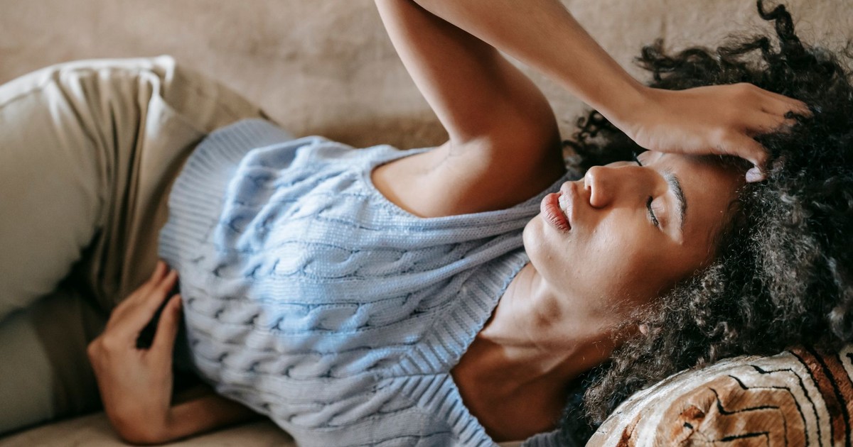 Young African American female lying on couch and touching forehead while having headache