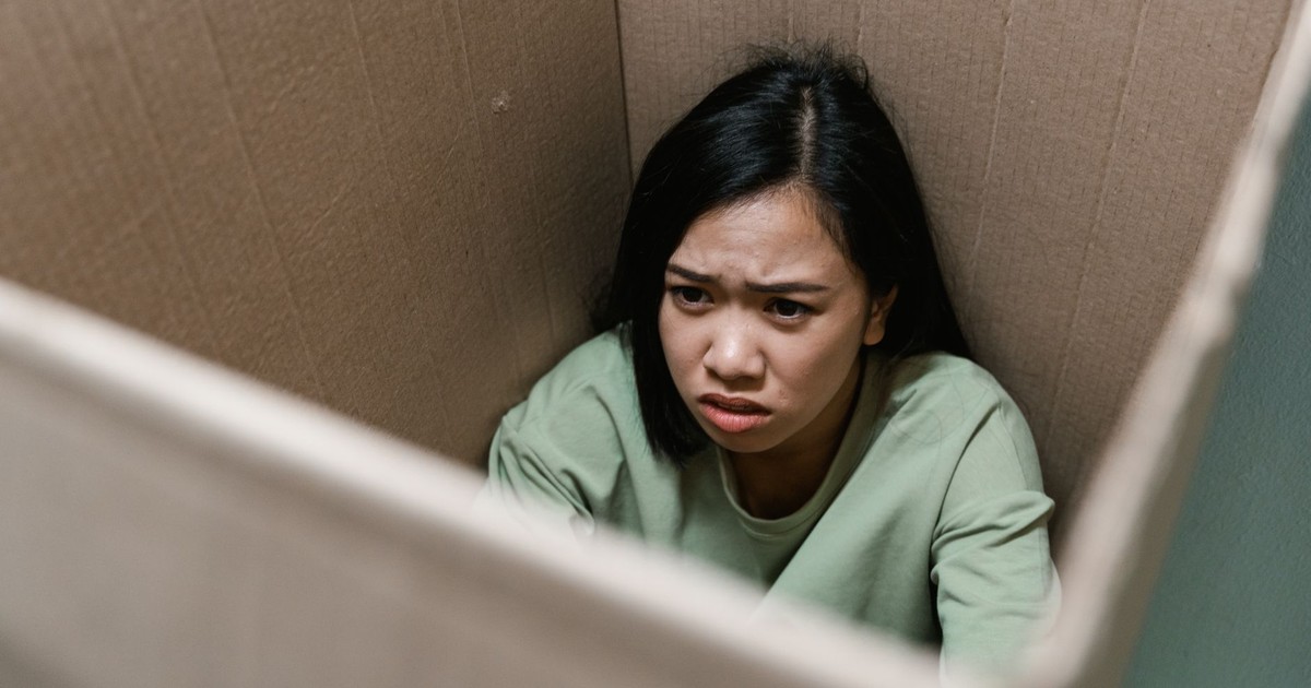 A woman inside a cardboard box showing a distressed expression, symbolizing anxiety or claustrophobia.
