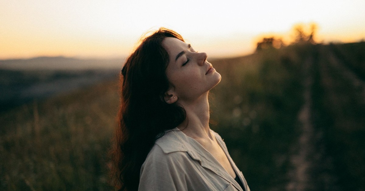 A serene woman with head tilted back, savoring the warm sunset in a field.