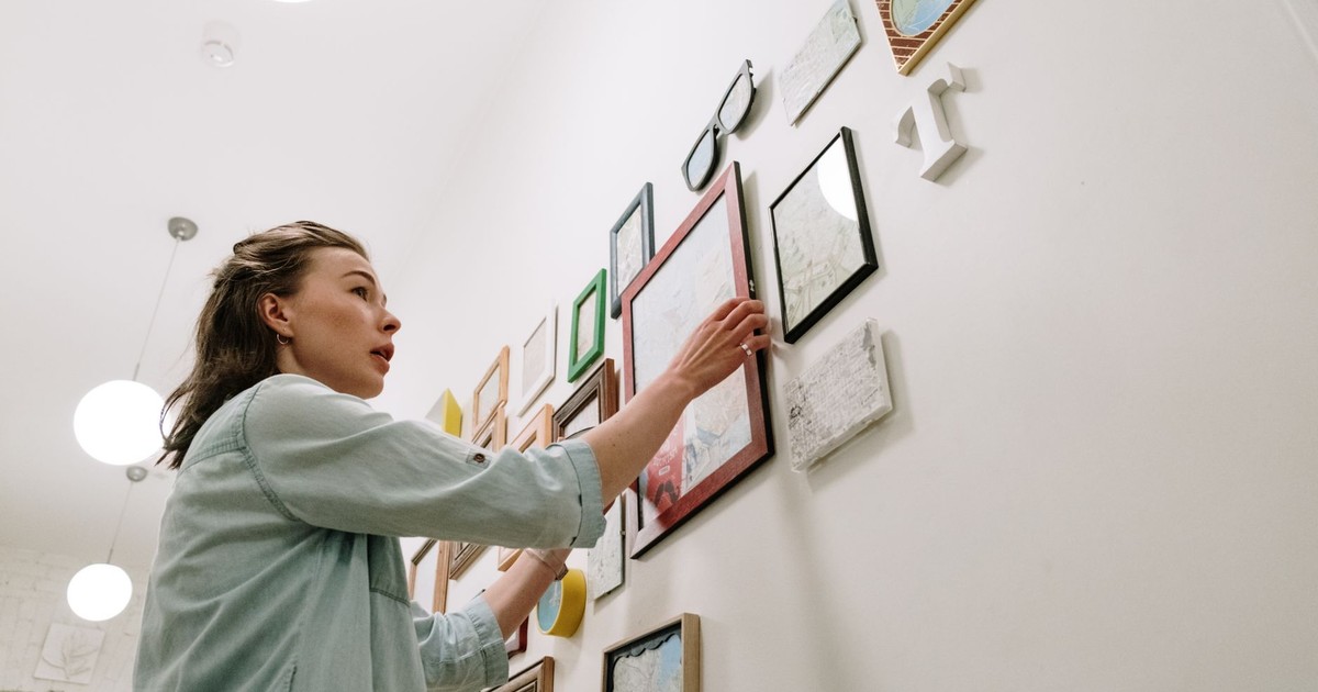 A woman arranging picture frames on a bright indoor wall.