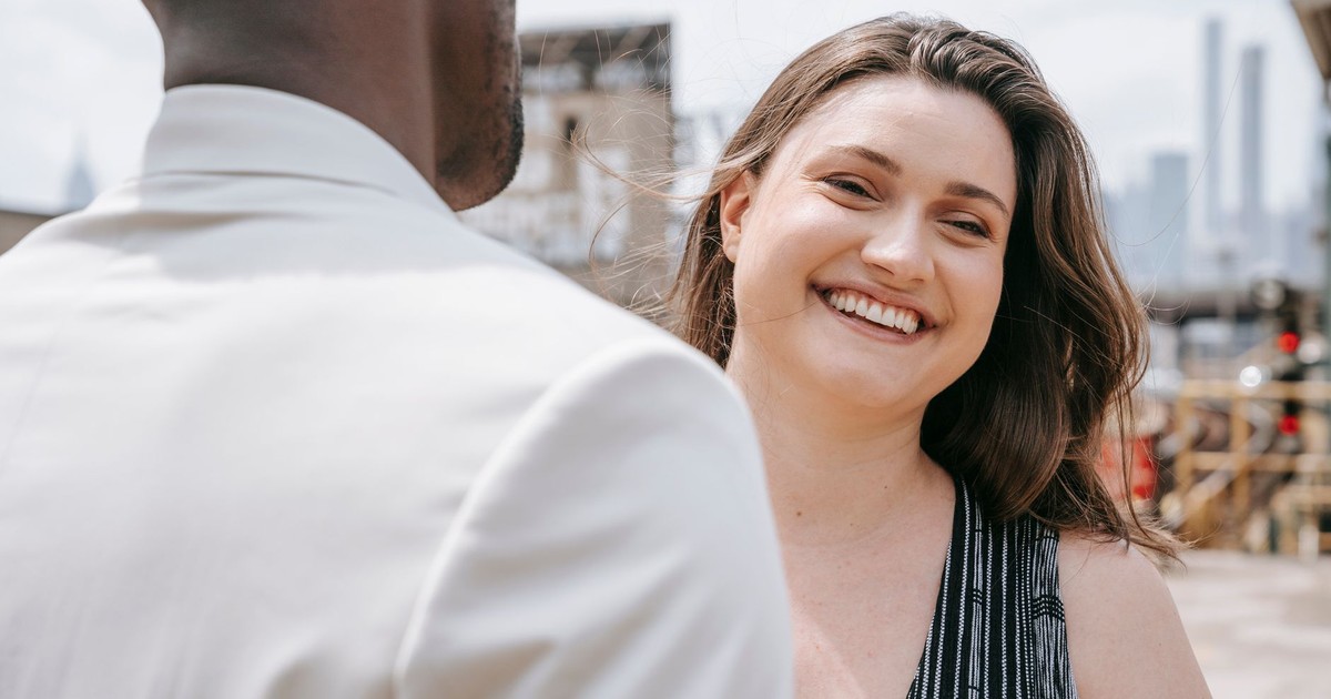 A joyful woman smiles while engaged in conversation outdoors on a sunny day.
