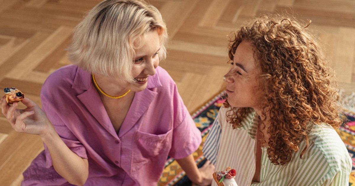 Two women sitting on the floor indoors, sharing desserts and enjoying a warm conversation.