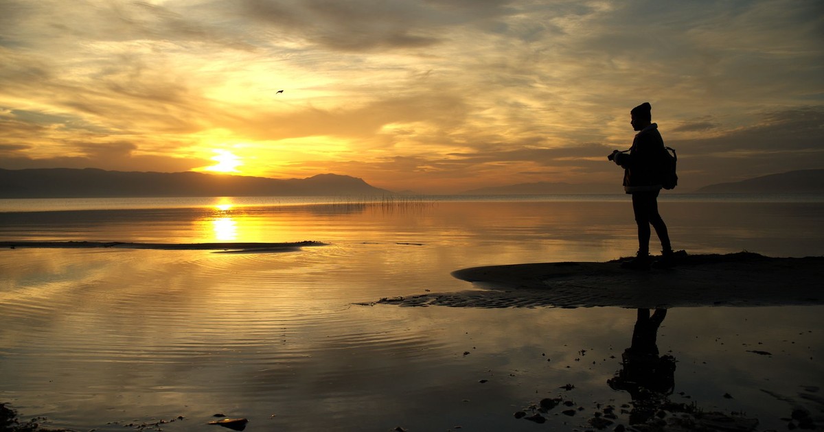 A stunning silhouette of a traveler by İznik Lake at sunset, capturing the serene reflections on the water.