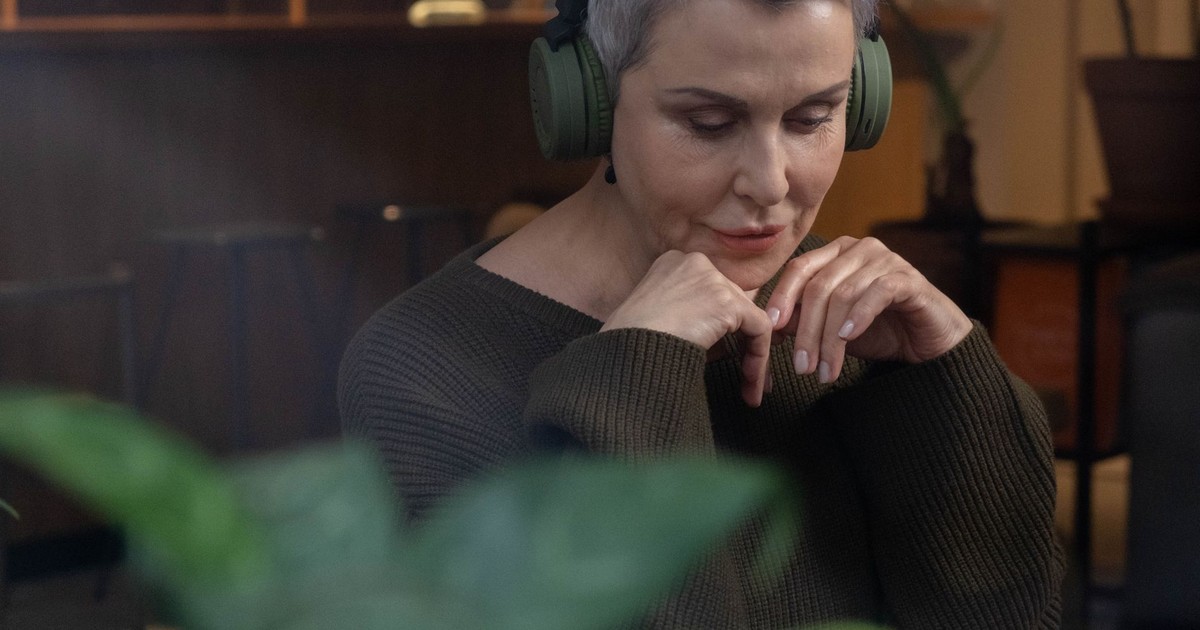 A senior woman wearing wireless headphones, relaxing indoors with a thoughtful expression.