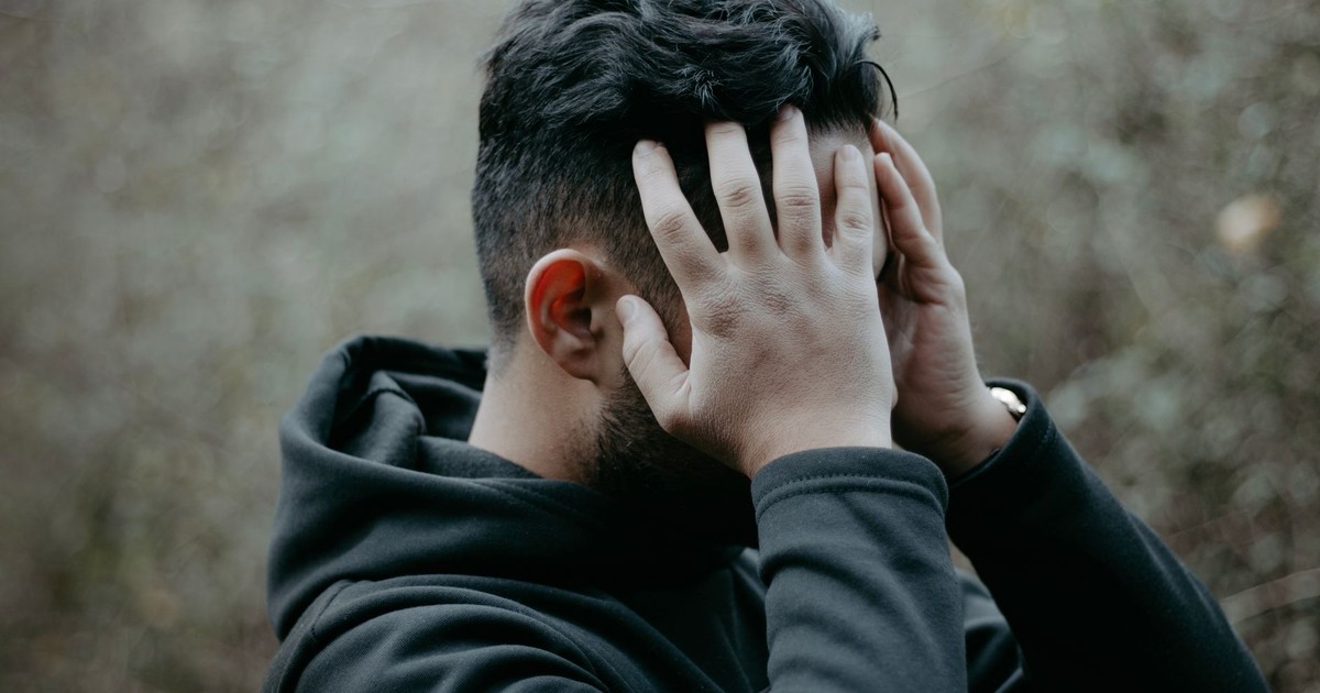 A man stands outdoors with his hands on his head, conveying stress and contemplation.