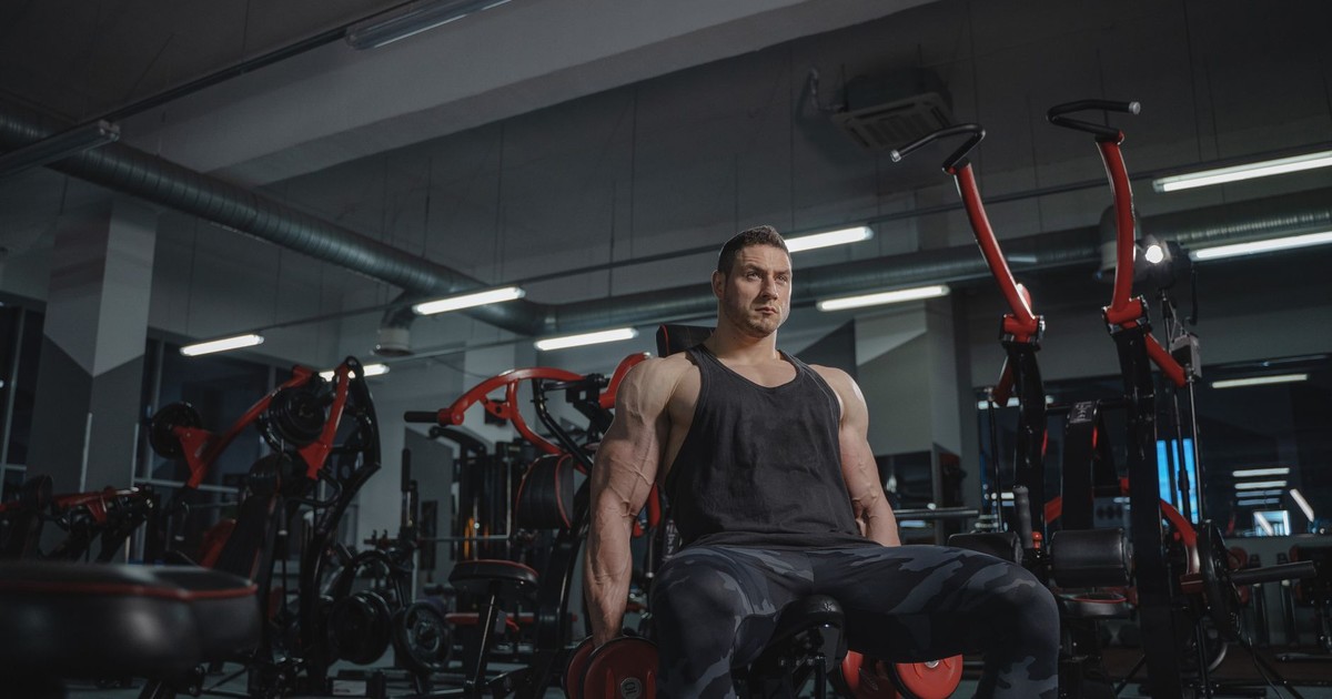Strong muscular man lifting dumbbells in a gym setting, showcasing power and fitness.