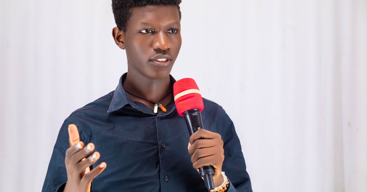 Confident young man presenting with a red microphone, wearing a dark shirt indoors.