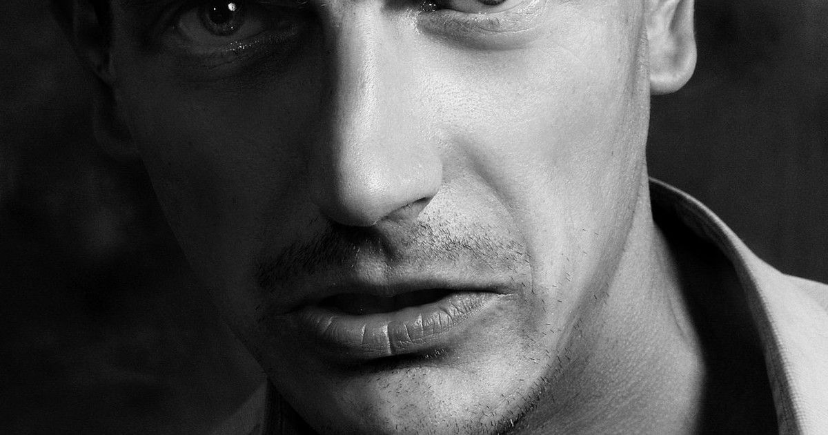 Close-up black and white portrait of a man with intense expression, highlighting facial features.