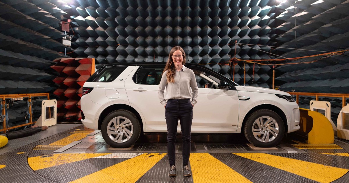 Female engineer stands in anechoic chamber with a car for sound testing.
