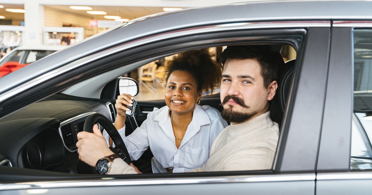 A smiling couple sitting inside a new car, holding the key and looking pleased.