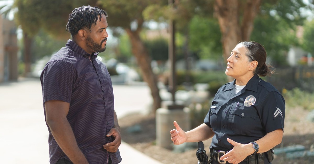 A police officer engaging warmly with a community member outdoors on a sunny day.