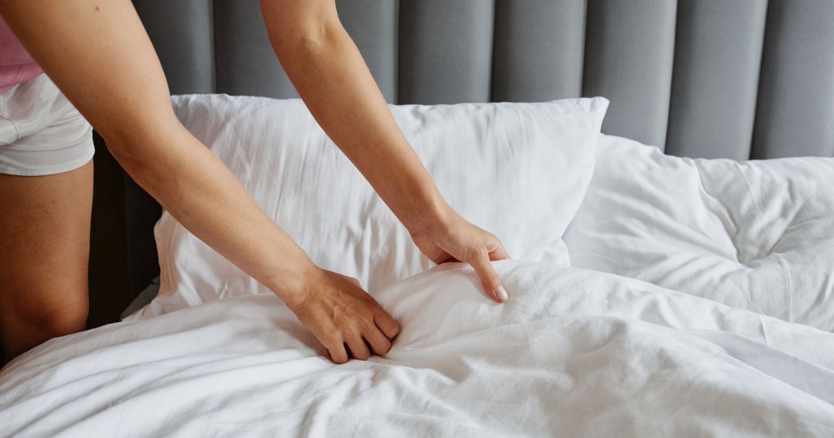 Close-up of a woman's hands making a bed with white sheets and pillows, creating a tidy look.