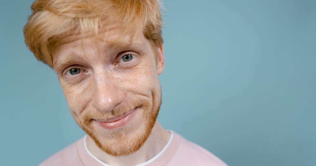 Cheerful bearded man with blonde hair smiling against a light blue background.